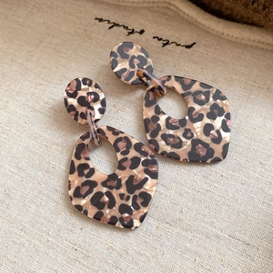 Detail of leopard print hollow geometric earrings on a beige linen background