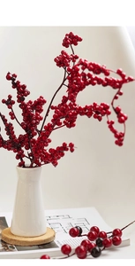 Artificial red berry branches in white ceramic vase on wooden coaster for Christmas decor
