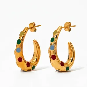 Macro shot of gold-plated C-shaped earrings with colorful enamel dot accents