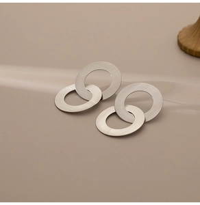 Détail de boucles d'oreilles entrelacées en métal argenté avec une texture mate