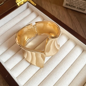 Wide gold asymmetric wavy open bangle bracelet with a high-polished metallic finish