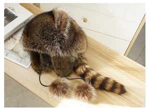 Detailed texture of brown faux fur raccoon hat with striped tail and pom-poms on wood