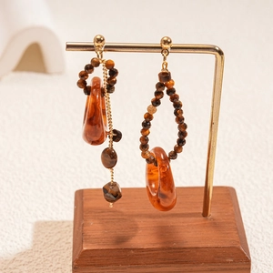 Detail of asymmetric resin earrings with golden metal accents and tiger eye beads
