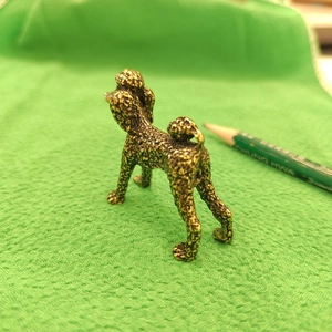 Antique brass miniature poodle statue with textured metal fur on a green surface