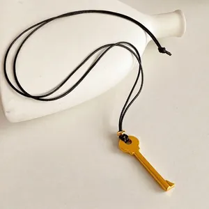 Collier avec pendentif clé dorée et cordon noir sur céramique blanche élégante