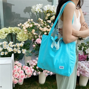 Detalle de bolso tote de lona azul con etiqueta tejida y correa de hombro a cuadros