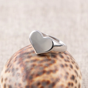 Close-up of polished heart-shaped stainless steel signet ring on a natural seashell