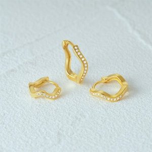 Close-up of golden wave hoop earrings with shimmering zircons on white texture