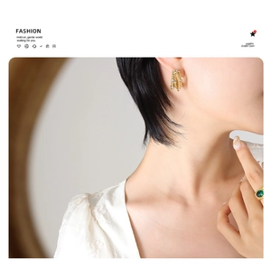 Detail of four-layer gold C-shaped earrings and green gemstone ring worn by a model