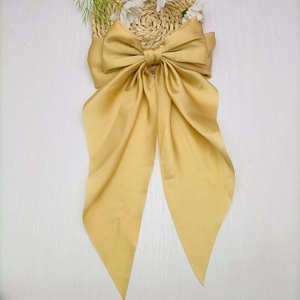 Close-up of a large champagne satin bow hair clip with ribbons on white wood background