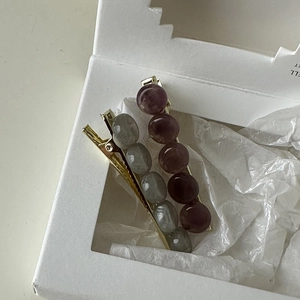 Detail view of two metal hair clips with grey-green and burgundy beads in a gift box