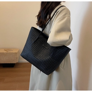 Side view of a large black woven tote bag worn over the shoulder with a beige trench coat