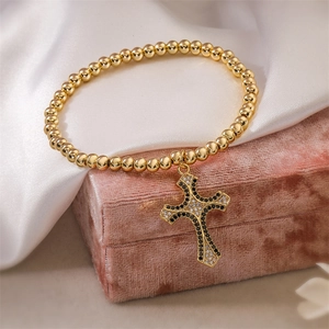 Detailed close-up of gold beaded bracelet with a black and white zircon cross pendant