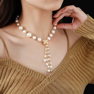 Detail of elegant faux pearl necklace featuring a golden clover and fringe tassel pendant