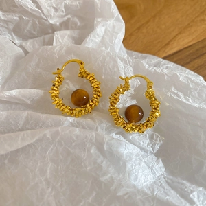 Detail of gold twisted rope hoop earrings with glossy brown resin beads on paper