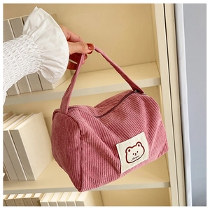 Pink corduroy makeup bag with cartoon bear patch held against a minimalist background