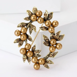 Vintage gold wreath brooch with enamel leaves, crystals, and golden pearls on white background