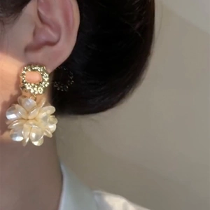 Close-up of gold-plated flower earrings with pearlescent petals on a model's ear