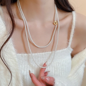 Detail of layered long pearl necklace with golden flower clasp on white sweater