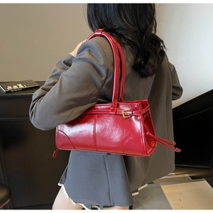 Detail of red glossy shoulder bag featuring dual straps and golden hardware buckles