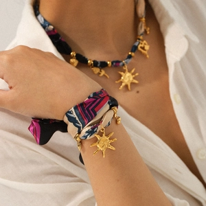 Close-up of golden sun face pendants on multi-color abstract print silk scarf jewelry