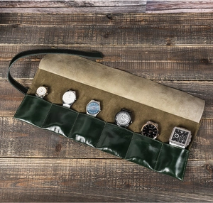 Vista piatta di un rotolo per orologi in pelle cerata verde scuro con 6 slot su legno