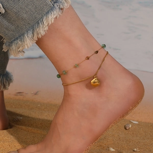 Detail of double-layer gold anklet with green beads and shell pendant on beach