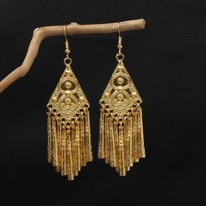 Detail of golden bohemian peacock earrings with bell tassels on a wooden branch
