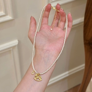 Detail einer Perlenkette mit goldenem Schaukelpferd-Anhänger an der Hand eines Models