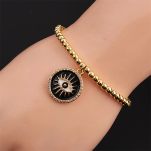 Détail d'un bracelet élastique en perles dorées avec pendentif œil en zircone au poignet