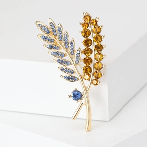Detail view of leaf-shaped brooch with blue and yellow rhinestones on white stand