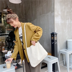Detail of cream canvas tote bag with yellow daisy floral print worn by a model in a blazer