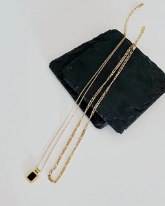 Detail of layered gold titanium steel necklaces with a black square pendant on dark rock