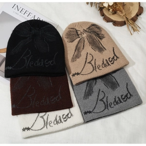 Close-up of knit beanies in black, brown, and grey with bow design on fabric