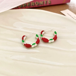 Close-up of silver apple-shaped enamel earrings set on a white textured plate