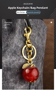 Detail of red glitter apple keychain with golden lobster clasp hanging on grey fabric