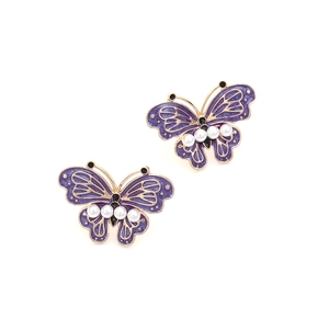 Detailed macro of gold-plated butterfly earrings with purple enamel and faux pearls