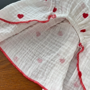 Close-up of white cotton gauze pet dress featuring red heart prints and red hem stitching