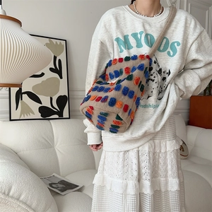 Close-up of plush bucket bag with colorful pompoms and off-white crossbody strap