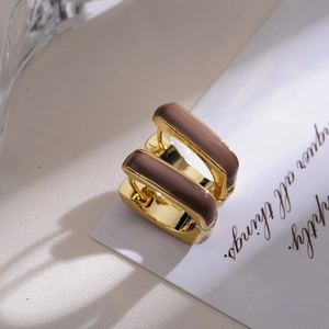 Modern square gold huggie earrings with brown enamel finish on silk background