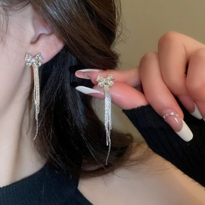 Détail de boucles d'oreilles nœud argentées avec strass et longues pampilles