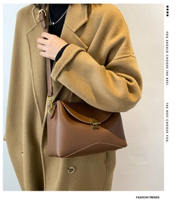Close-up of a brown leather crossbody bag with a square metal buckle on a wool coat