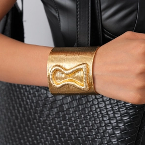 Macro shot of gold wide cuff bracelet with linear texture and hourglass metal detail