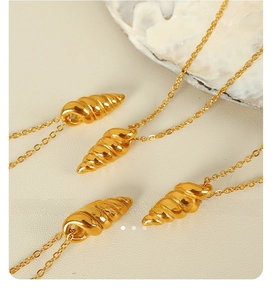 Close-up of four gold spiral conch pendant necklaces on a beige leather display pad