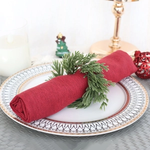 Close-up of red linen napkin with pine branch napkin ring on festive gold patterned plate