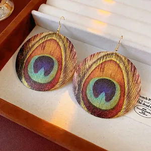 Bohemian round earrings with peacock feather pattern and gold hooks in a jewelry box