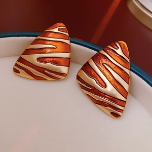 Detailed close-up of golden triangle earrings with orange striped enamel in a jewelry box