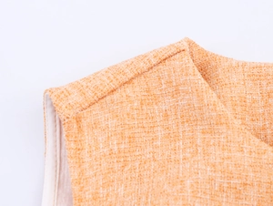 Détail de la texture du tissu en tweed orange et couture d'épaule du gilet court