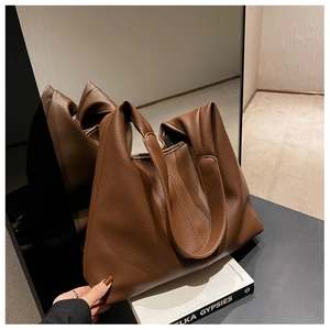Detail of a brown lychee pattern leather tote bag placed on a book in a minimalist setting