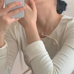 Close-up of minimalist 925 sterling silver bow bracelet on model's wrist with soft lighting